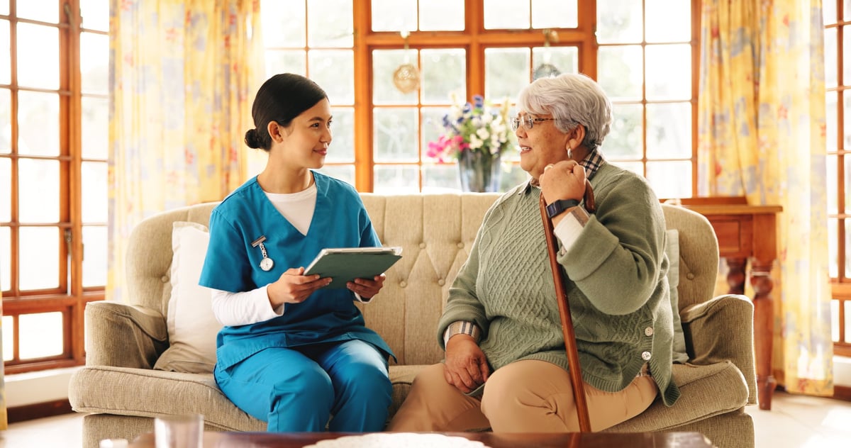 A caregiver and an older woman reviewing information together on a tablet in a bright living space