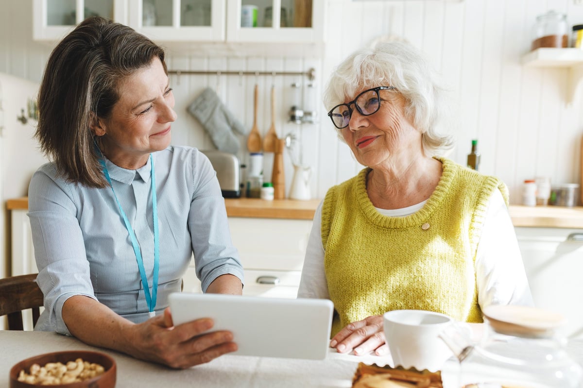 A specialist working warmly with an older woman on a tablet game at a kitchen table