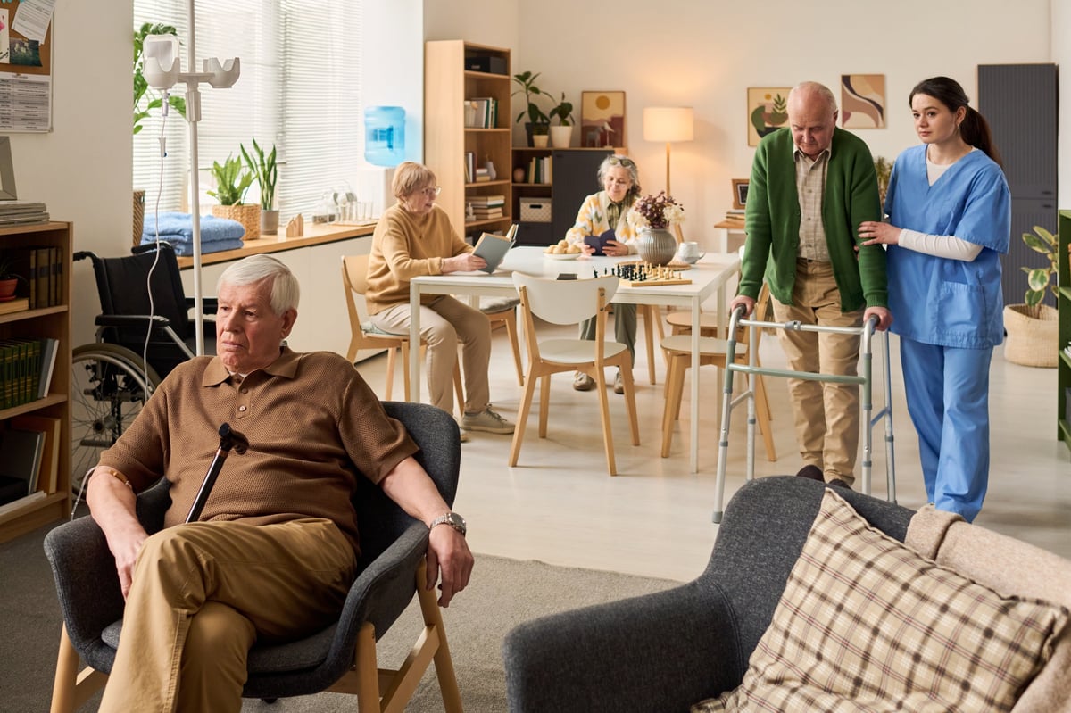 A young adult caregiver supporting a senior man using a walker in a warm residential setting